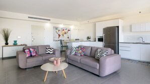 A modern living room with two sofas, a coffee table, and a kitchen area with a refrigerator and cabinets. - MAMAD Deluxe Apt & Terrace with City Overview by FeelHome (Holon)