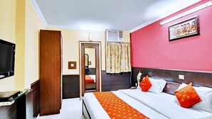 A hotel room with a bed, a television, a desk, and a door leading to a bathroom. - Hotel Mantri Residency (Nagri)