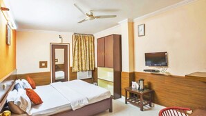 A hotel room with a bed, a wardrobe, a television, a ceiling fan, and a small table with a kettle. - Hotel Mantri Residency (Nagri)