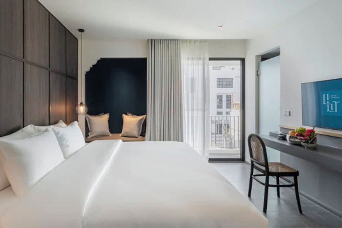 Habitación de hotel con una cama grande, un escritorio con silla, televisor y vista a la ciudad.