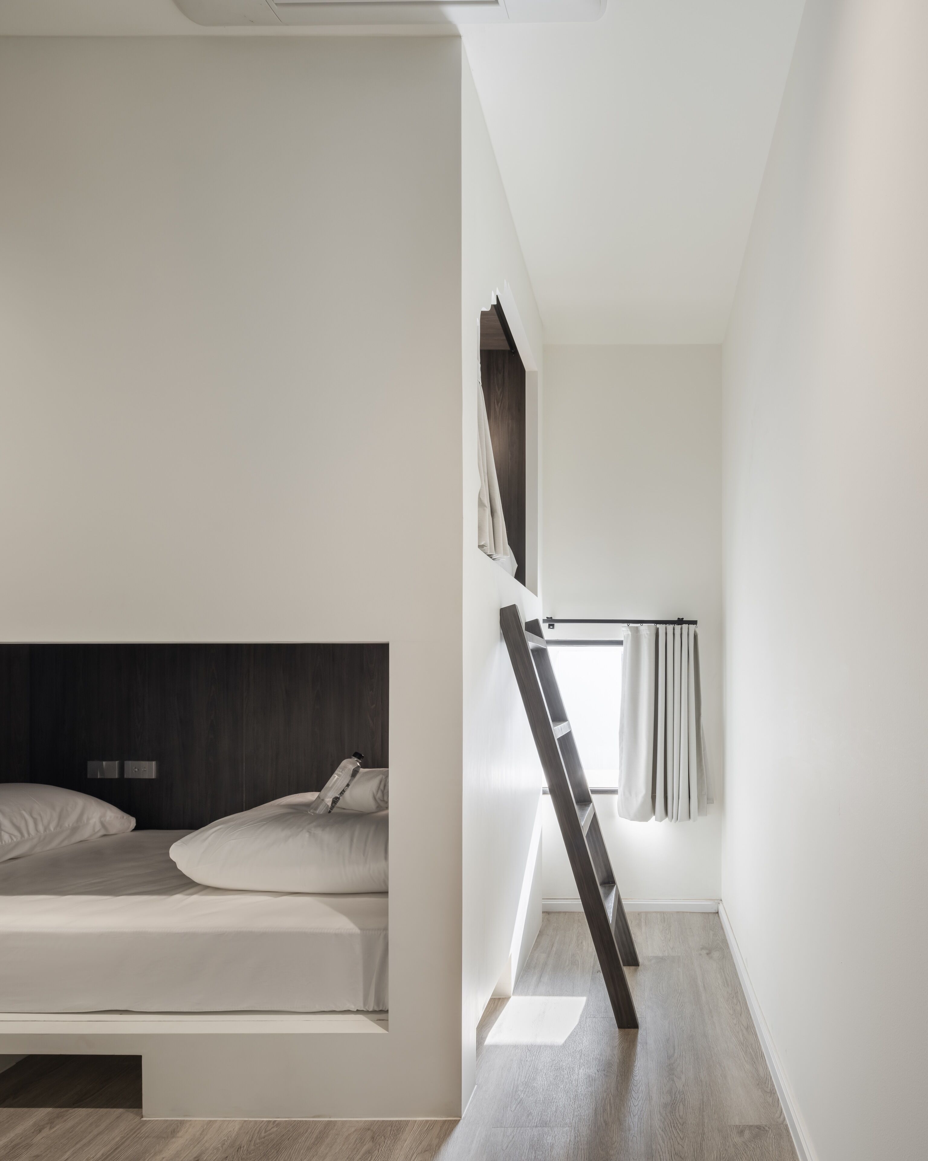 A modern, minimalist bedroom with a bunk bed, a ladder, and a window with curtains.