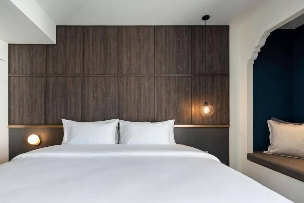 Habitación de hotel con una cama grande, cabecera de madera, dos lámparas de noche y ventana con vistas.