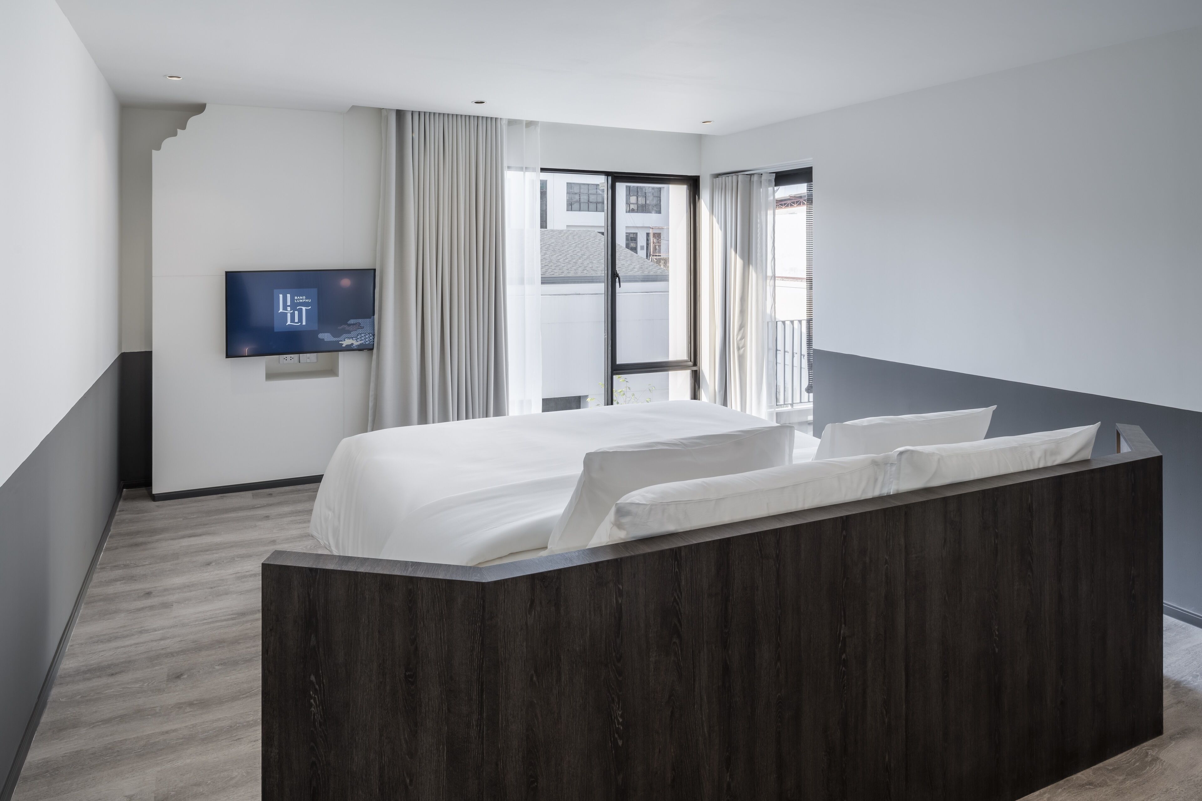 A modern hotel room with a large bed, a flat-screen TV mounted on the wall, and a view of the outside through a large window.