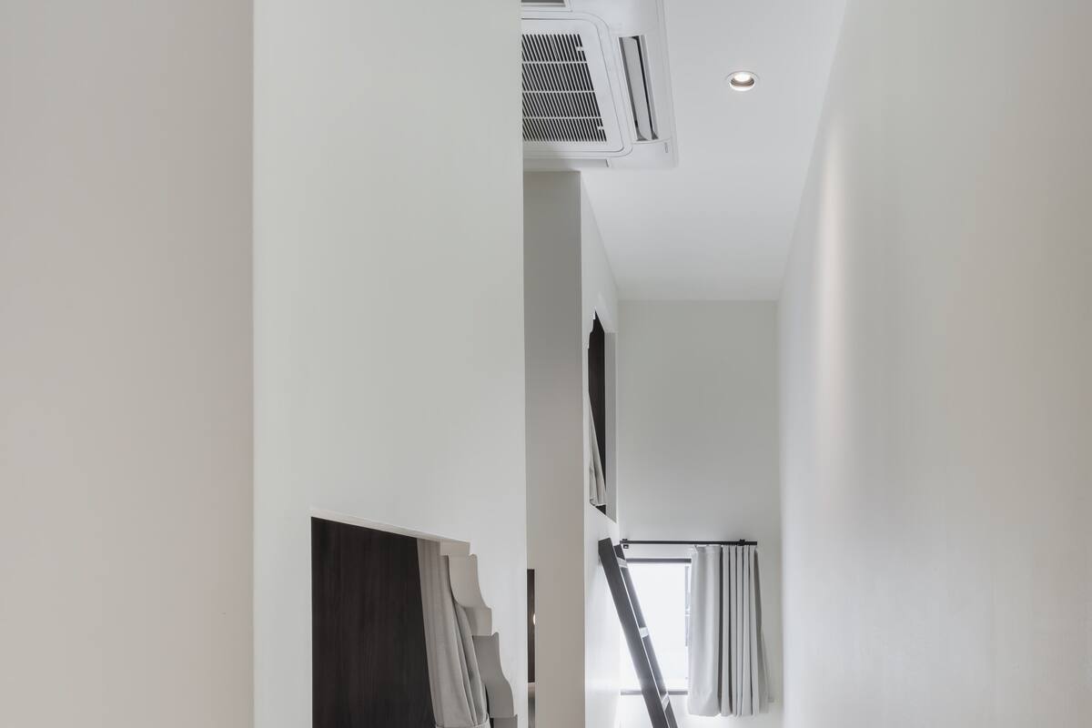 Una habitación estrecha y bien iluminada con una cama litera, un ventanal con cortinas y un radiador en la pared.
