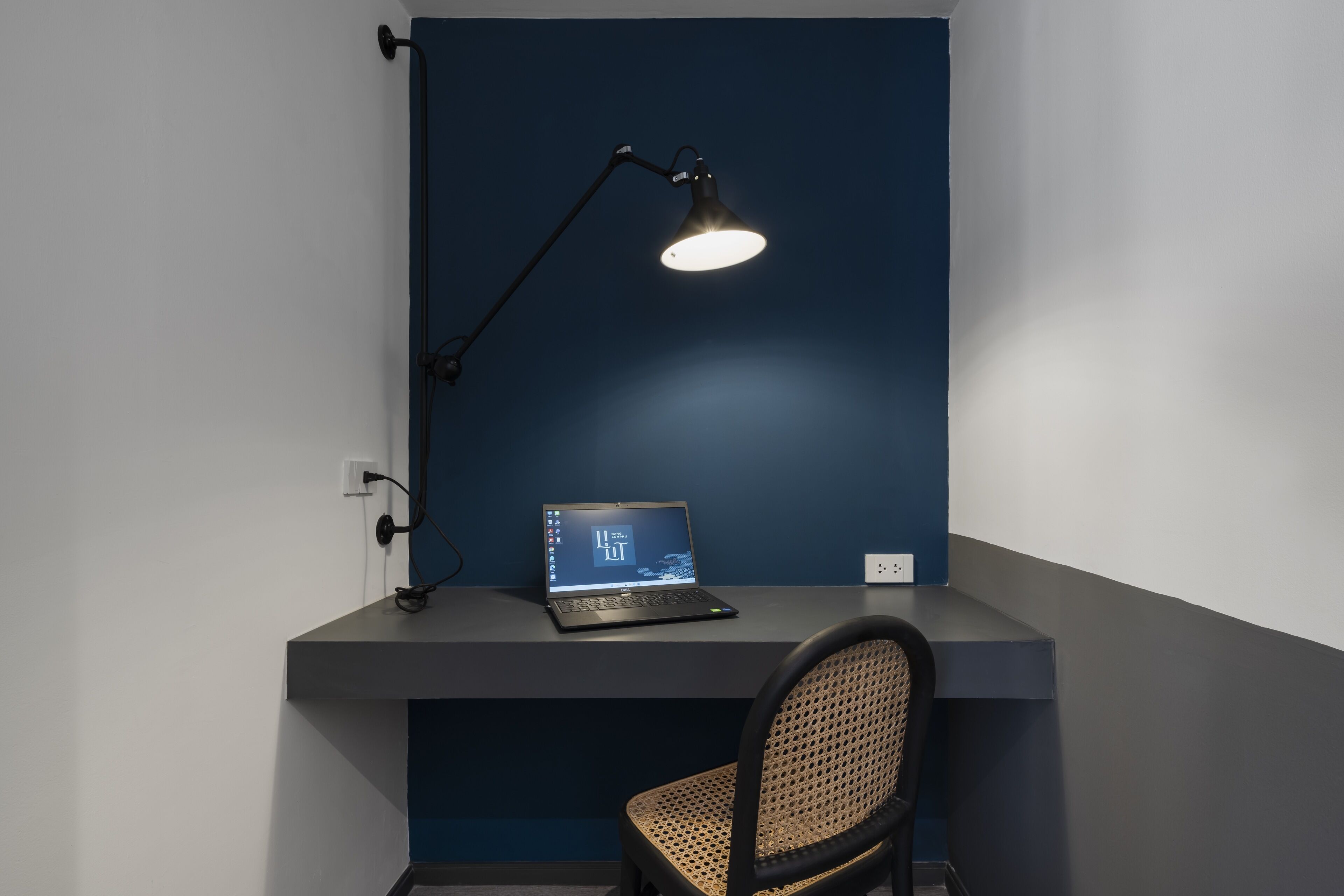 A desk with a laptop, a desk lamp, and a chair in a room with dark blue walls.