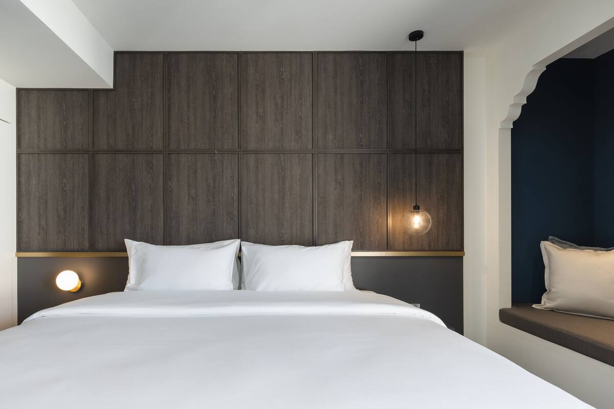 Un dormitorio moderno con una cama grande, cabecera de madera, lámparas de noche y un banco empotrado con cojín.