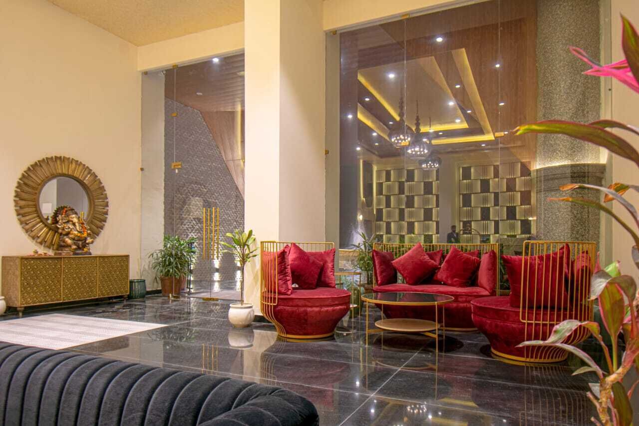 A modern lobby with a black leather sofa, red cushioned chairs, a gold-framed mirror, and a large statue.