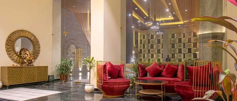 A modern lobby with a black leather sofa, red cushioned chairs, a gold-framed mirror, and a large statue.