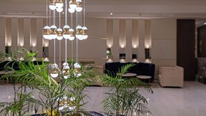 Un hall con una lámpara de araña moderna, plantas en macetas y una alfombra estampada.