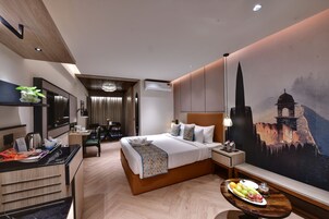A modern hotel room with a large bed, a dining area, a TV, and a mural of a castle.