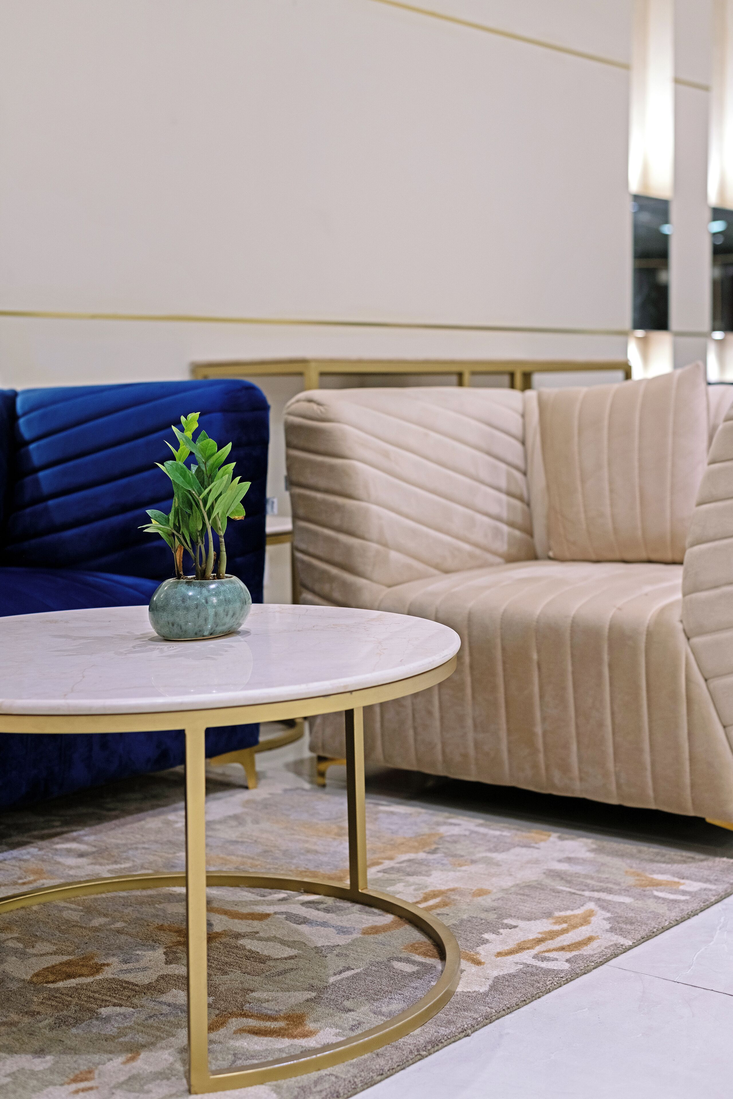 Een ronde tafel met een vaas groene planten, een blauwe bank en een beige bankstel in een modern interieur.