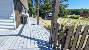 Une terrasse en bois avec une poubelle, un véhicule garé à l’arrière-plan et une clôture en bois.