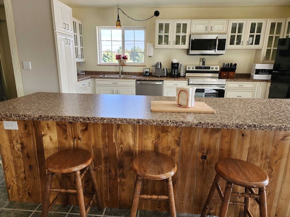 A kitchen with white cabinets, a granite countertop, a stainless steel microwave, and a wooden island with stools.