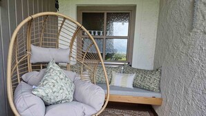 A wicker hanging chair with cushions, a cushioned bench, and a patterned rug in a cozy corner.