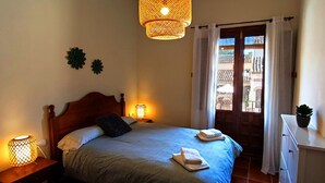 Ein Schlafzimmer mit einem Bett, zwei Wandlampen, einem Fenster mit Vorhängen und einer Zimmerpflanze auf einem Nachttisch.