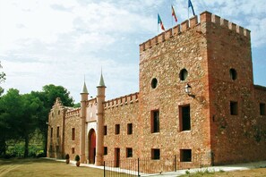 Ein historisches Steinhaus mit einem zentralen Turm, Rundbogenfenstern und einer Fahnenstange.