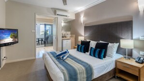 Een hotelkamer met een bed, nachtkastje, lamp en een televisie waarop een strandafbeelding te zien is.