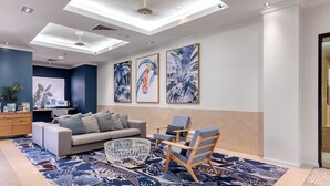 Een moderne woonkamer met een bank, fauteuils, een salontafel en een kamerbreed tapijt. Er zijn plafondlampen en kunstwerken aan de muur.
