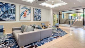 Een moderne lobby met een grijze bank, een blauw gestreept vloerkleed en tropische kunstwerken aan de muren.