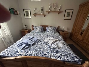 Un lit bien fait, avec une literie à motifs, deux tables de chevet avec des lampes, une armoire en bois et des étagères murales ornées d’objets décoratifs.
