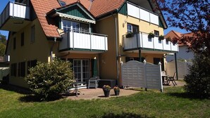 A two-story house with a red-tiled roof, a balcony, and a fenced yard.