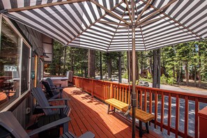A wooden deck with Adirondack chairs, a wooden bench, and a striped umbrella. - Chapel Haus by Hauserman Rental Group (Tahoe City)