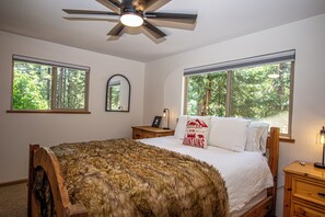 Ein Schlafzimmer mit einem großen Bett, zwei Fenstern, einem Deckenventilator, einem Nachttisch und einem Spiegel.