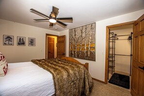 Ein Schlafzimmer mit Bett, Deckenventilator, Kleiderständer und einer Tür zu einem anderen Raum.