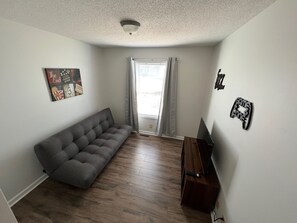 A room with a grey sofa, a wooden TV stand, and a ceiling light.