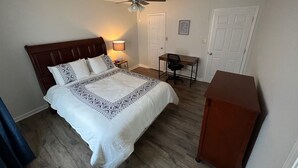 Un dormitorio con cama, escritorio, silla, ventilador de techo y una puerta.