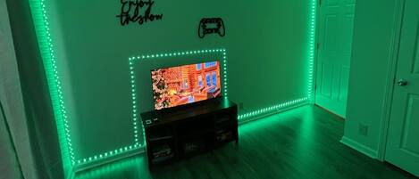 A room with green LED strip lighting along the walls, a television on a wooden stand, and a door to the right.