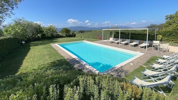 Ein rechteckiger Pool mit glasklarer, blauer Wasseroberfläche, umgeben von einem gepflegten Rasen und einer Reihe weißer Liegestühle.
