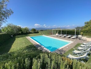 Une piscine rectangulaire à l’eau d’un bleu limpide, entourée d’une pelouse bien entretenue et bordée d’une rangée de chaises longues blanches.