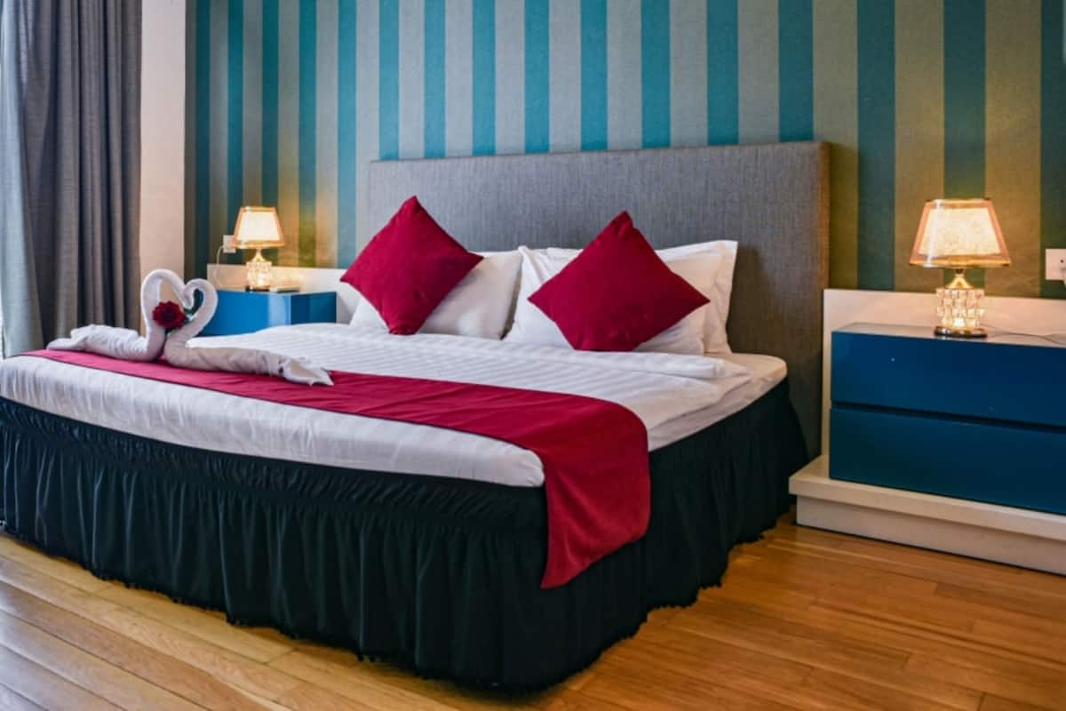 A hotel room with a large bed, striped wallpaper, and two bedside tables with lamps.