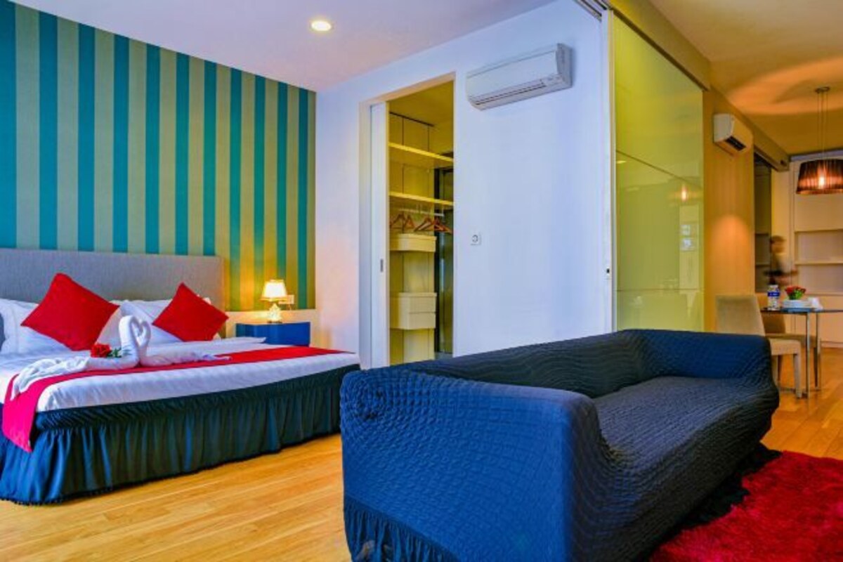 A hotel room with a bed, a blue sofa, a red rug, and a wardrobe.