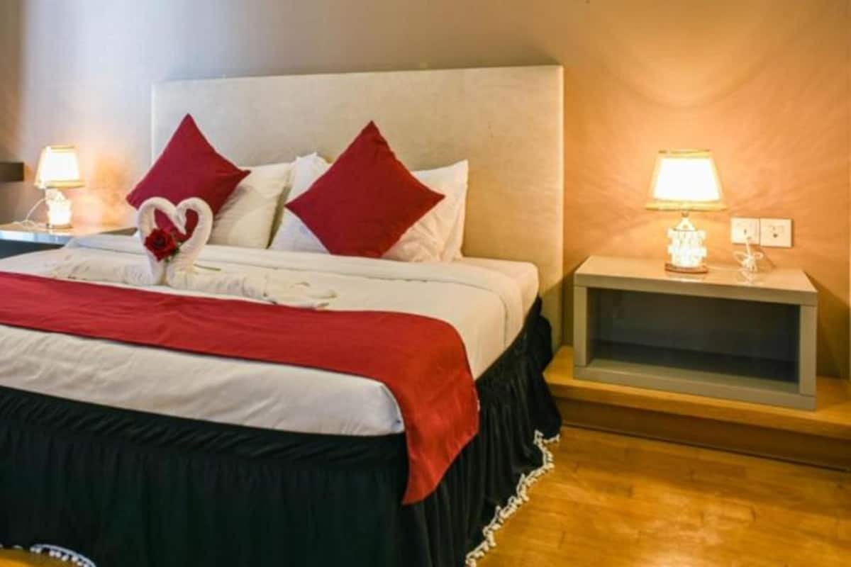 A hotel room with a bed, red pillows, a heart-shaped towel decoration, bedside lamps, and a nightstand.