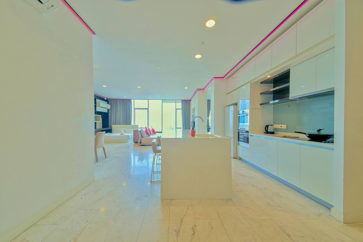 A modern kitchen with white cabinets, a central island, and a dining area with a sofa and chairs.