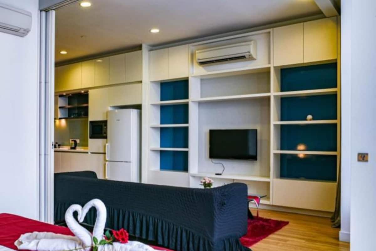 A hotel room with a bed, a TV, a kitchenette, and a bathroom.