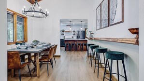 Une cuisine moderne avec un plafond en bois, un coin repas avec une table et des chaises en bois, et un bar avec des tabourets.