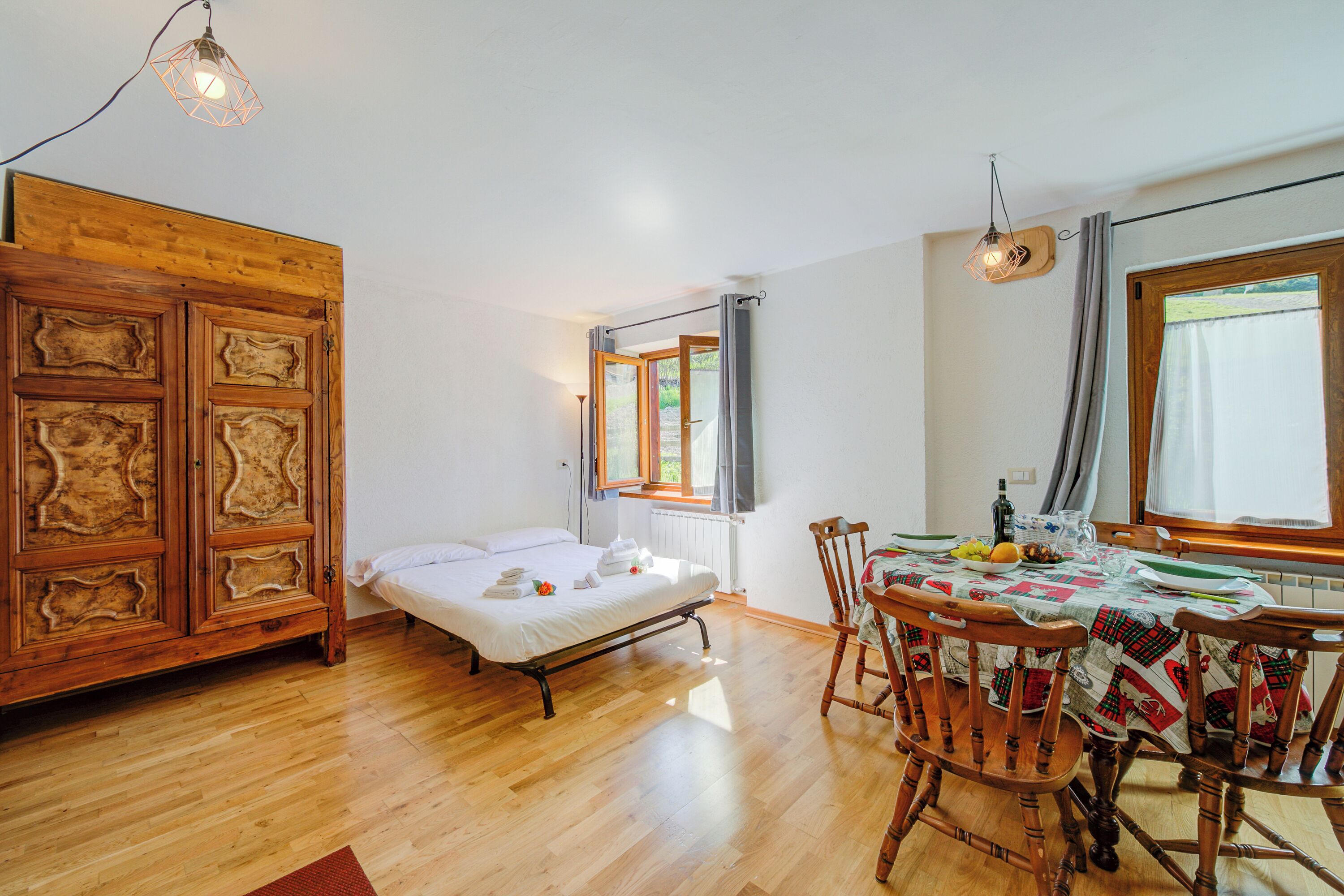 Een kamer met een houten bed, een eettafel met stoelen en een raam met gordijnen.