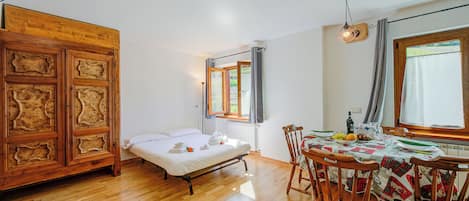 Una habitación con una cama de madera, una mesa de comedor con sillas y un ventanal con cortinas.
