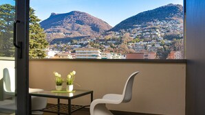 Un balcon agrémenté d’une chaise moderne, d’une petite table avec des plantes en pot et offrant une vue sur une ville située sur une colline.