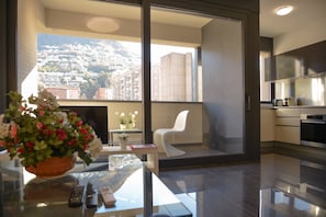 Una cocina moderna con un ventanal grande, un balcón con una silla blanca y vistas a una colina.