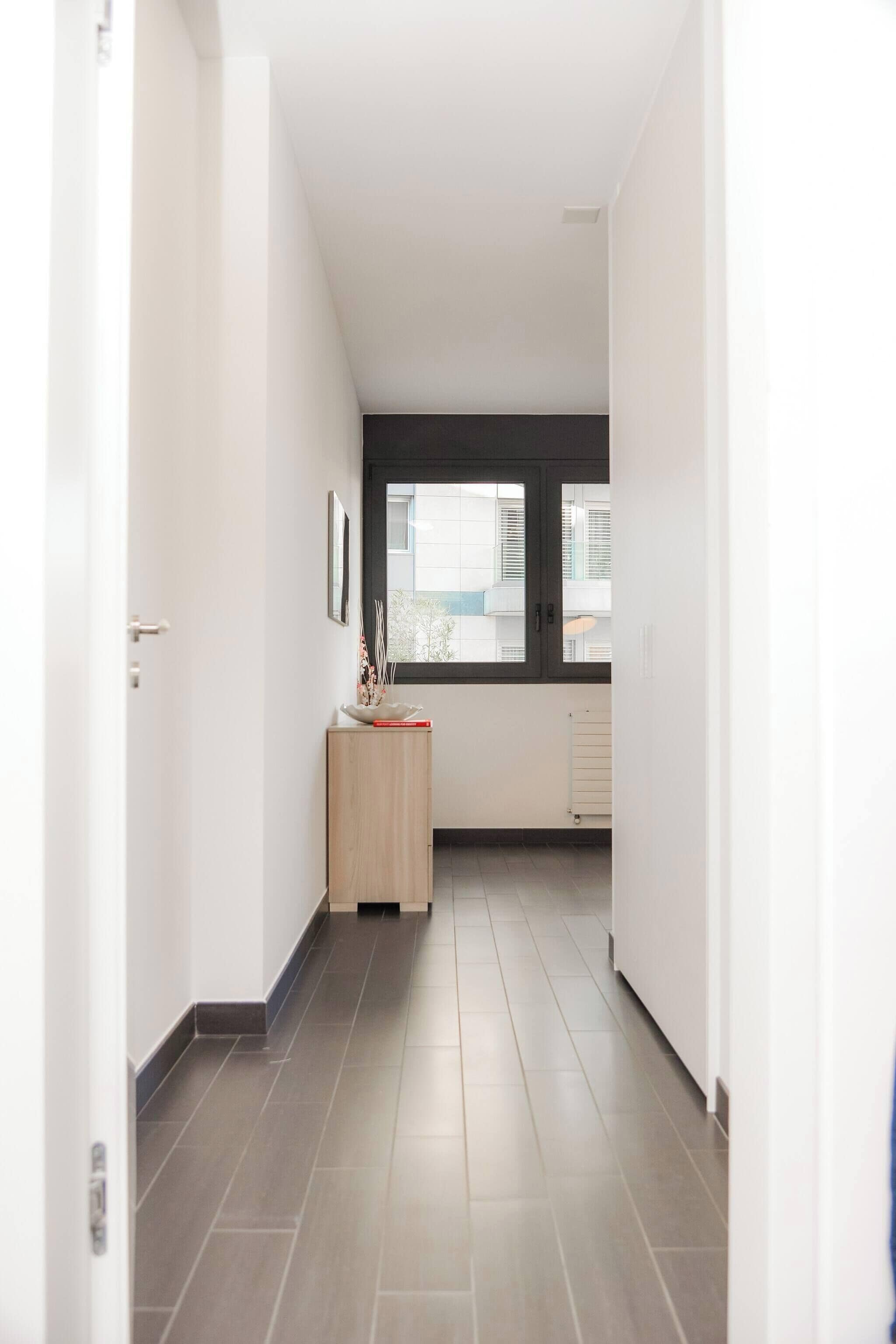 A narrow hallway with a wooden cabinet and a window.