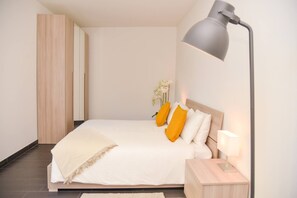 Un dormitorio moderno con cama, mesita de noche, lámpara y espejo.