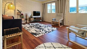 Ein Wohnzimmer mit Sofa, einem Sessel, einem Fernseher, einem Couchtisch und einem gemusterten Teppich.