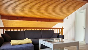 Una sala de estar moderna con techo de madera, un sofá gris con una manta amarilla y una mesa de centro blanca.
