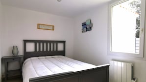 Un dormitorio con cama, mesita de noche, radiador y ventana con vistas al exterior.
