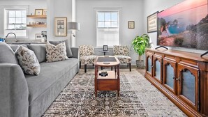 Un salon avec un canapé gris, des coussins à motifs, une table basse, un téléviseur et un meuble.