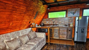 A cozy cabin-style kitchen with a wooden floor, a built-in microwave, a refrigerator, and a wooden bench. - Hakuna Matata glamping (Monguí)